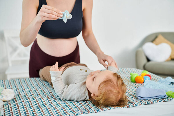 A baby calmly rests on a bed beside a young, beautiful mother, showcasing a tender moment of motherly care and love.