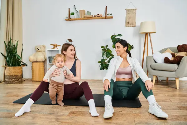 两名妇女和一名婴儿在家里的一个五颜六色的垫子上 在一位支持他们的教练的指导下 一起享受轻松的瑜伽课 — 图库照片