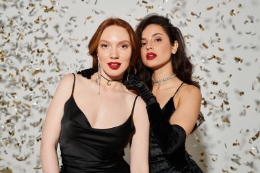 İki zarif kadın gülümsüyor, konfeti önünde sevinçle poz veriyorlar..