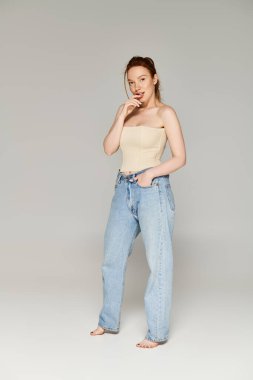 Casual yet chic, a woman in a tank top and jeans poses confidently for the camera. clipart