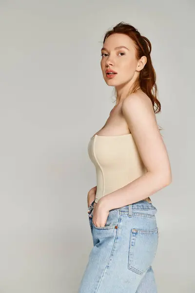 stock image A woman in a tan top and blue jeans poses elegantly.