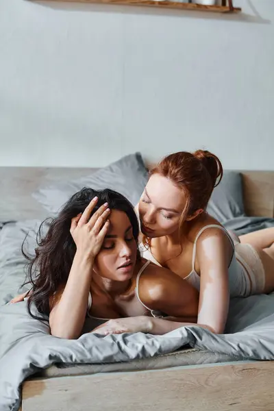 Two sophisticated women in elegant attire laying serenely on a bed together.