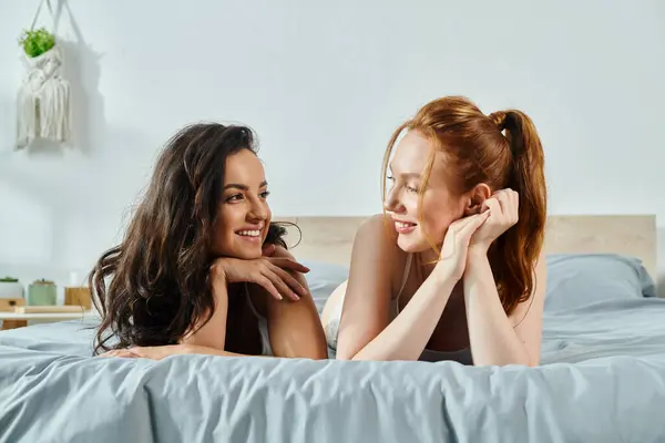 Two elegant women in formal attire reclining on a bed, exuding love and happiness.