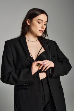 Stylish plus size woman striking a pose in a black suit and a bold choke necklace against a gray backdrop. clipart
