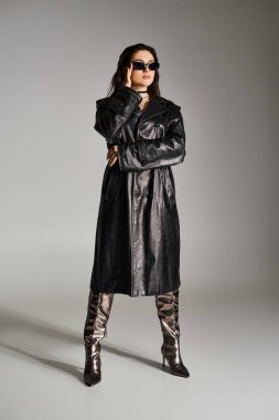A plus size woman exudes confidence in a stylish black leather coat and boots against a gray backdrop. clipart