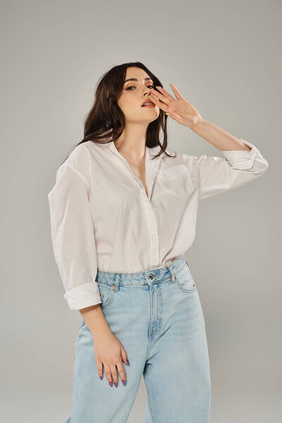 A beautiful plus size woman poses confidently in a white shirt and jeans against a gray backdrop.