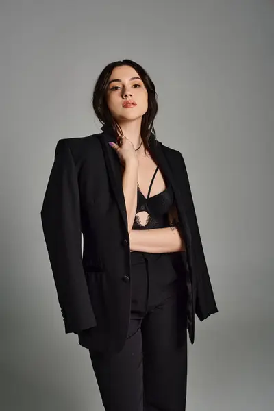 stock image A beautiful plus-size woman poses confidently in a stylish black suit against a gray backdrop.