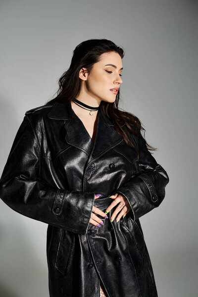 A stunning plus size woman poses confidently in a chic black leather coat on a gray backdrop.