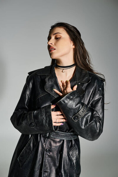 A beautiful plus-size woman strikes a pose in a sleek black leather jacket and trendy choker against a gray backdrop.