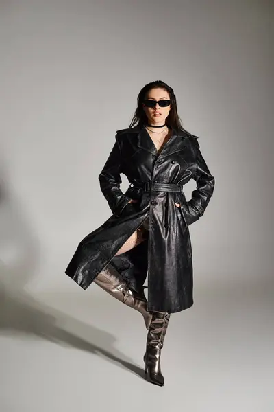 黒いコートとサングラスのスタイリッシュなプラスサイズの女性は グレーの背景に自信を持ってポーズ — ストック写真