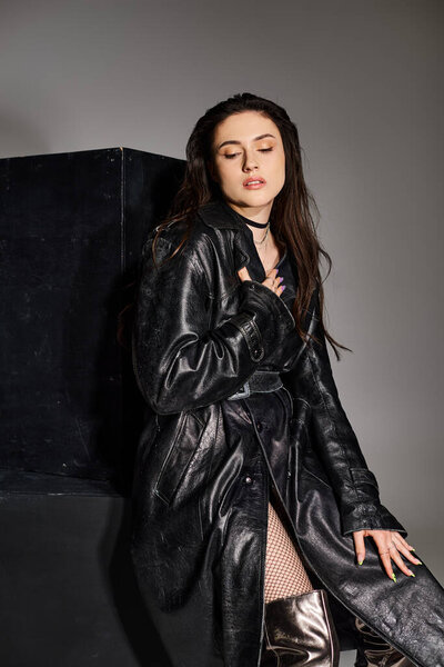 A beautiful plus size woman poses in a sleek black jacket and shiny silver boots against a gray backdrop.