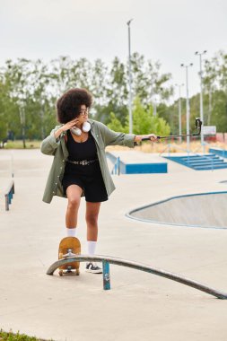 A young African American woman with curly hair skillfully rides a skateboard along a rail in a vibrant outdoor skate park. clipart