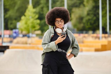 A stylish woman with a voluminous afro hairdo holding a cell phone in hand. clipart