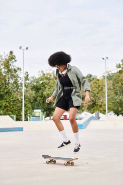 Young African American woman with curly hair skateboarding in a skate park on a cement surface. clipart