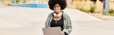 Afro saçlı bir kadın dizüstü bilgisayar tutuyor, teknoloji ve kültürü birleştiriyor..