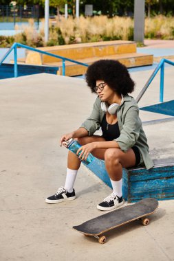 A young African American woman with curly hair sitting elegantly on a bench while holding a bottle of water in a skate park. clipart