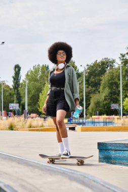 Genç, kıvırcık saçlı, Afro-Amerikalı bir kadın kaykay pistinde kaykay yapıyor..