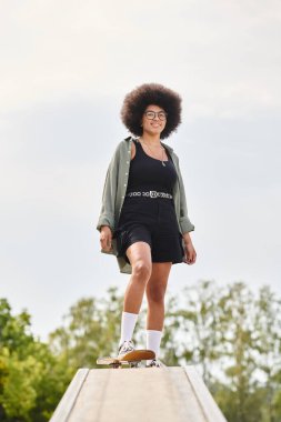 Afro saçlı genç Afrikalı Amerikalı bir kadın kaykay pistinde zarif bir şekilde kaykay yapıyor..