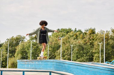 Açık hava kaykay parkında havuzun kenarında ustaca kıvırcık saçlı genç bir Afrikalı Amerikalı kadın..