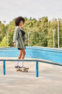 Kıvırcık saçlı genç Afrikalı Amerikalı kadın kaykay kullanıyor. Açık hava kaykay parkında metal korkuluklarda korkusuzca kayıyor..