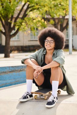 Şehvetli bir afro saçı olan şık, genç bir Afrikalı Amerikalı kadın canlı bir kaykay parkında kaykayın üzerinde oturuyor..