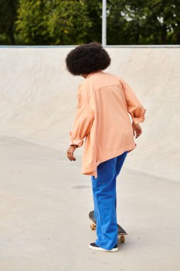 Kıvırcık saçlı Afro-Amerikalı bir kadın açık hava kaykay parkında kaykay sürüyor..