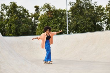 A young African American woman with curly hair confidently rides her skateboard up the side of a ramp in a skate park. clipart