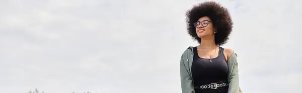 stock image A vibrant woman with an afro standing gracefully in a lush field, exuding confidence and freedom.