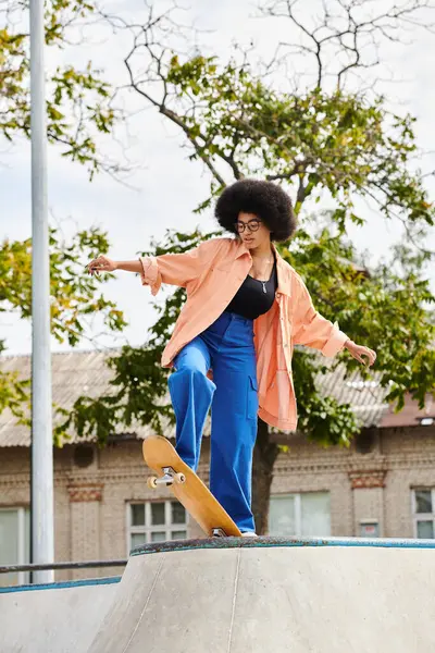 stock image A young African American woman with curly hair skillfully rides a skateboard up the side of a ramp at an outdoor skate park.