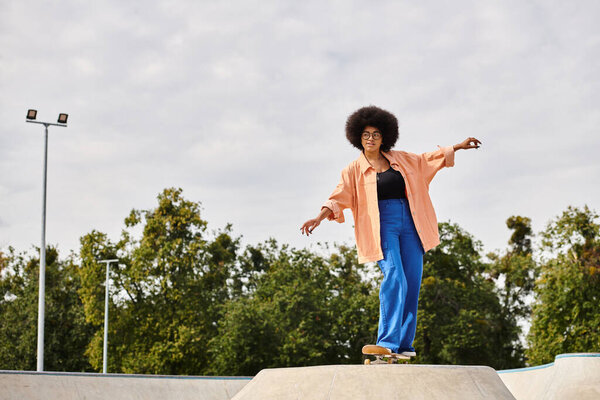 Young African American woman with curly hair skateboarding on top of a cement ramp in a skate park.