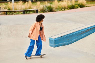 Genç bir Afro-Amerikalı kadın, kıvırcık saçlı kaykay kaykayı stili ve kendine güveni olan bir kaykay parkında..