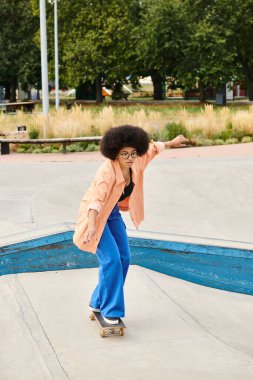 Young African American woman with curly hair rides skateboard down cement ramp at outdoor skate park. clipart