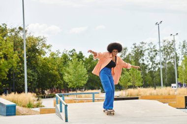 Young African American woman with curly hair skillfully rides a skateboard on a ramp at an outdoor skate park. clipart