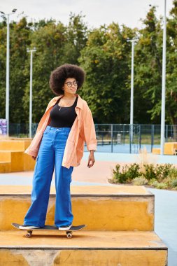 A young African American woman with curly hair confidently stands atop a skateboard ramp in an outdoor skate park. clipart