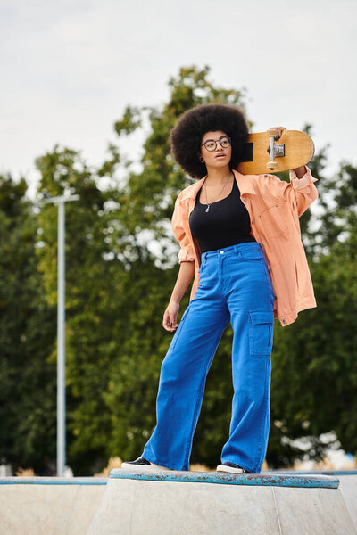 A young African American woman with an afro showcases her skills while elegantly holding a skateboard at a skate park.