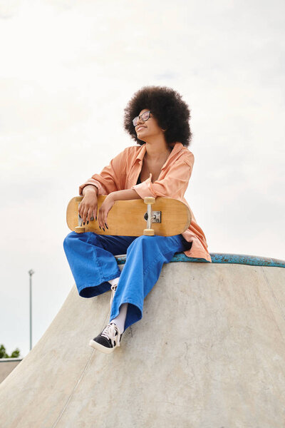 A young African American woman with curly hair sitting confidently on top of a skateboard ramp.