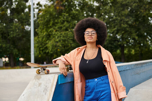 A young African American woman with curly hair stands confidently next to a skateboard on a skate park ramp.