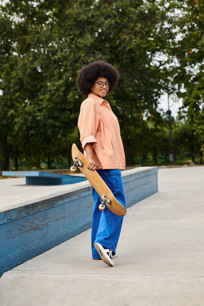A young man of African descent with curly hair confidently holds a skateboard in a vibrant skate park setting.