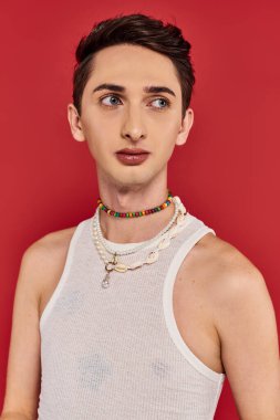 Modayı takip eden, gündelik giysiler içinde kırmızı arka planda duran ve başka yöne bakan gay bir adam.