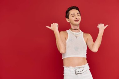 Kırmızı arka planda aksesuarları olan sıradan giyinmiş neşeli, modaya uygun eşcinsel bir adam.