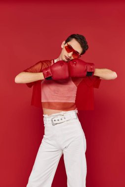 Güneş gözlüklü, kırmızı balık ağlı, boks eldivenli ve kameraya bakan çekici bir gay.