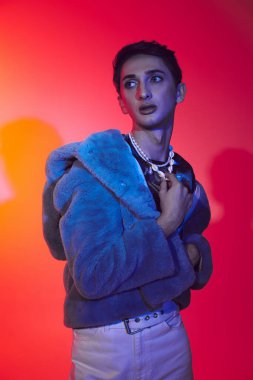 Mor sahte kürklü yakışıklı, çift cinsiyetli adam canlı arkaplanda poz veriyor ve başka tarafa bakıyor.