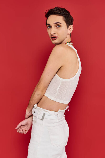 attractive gay man in casual attire with accessories posing on red background and looking at camera