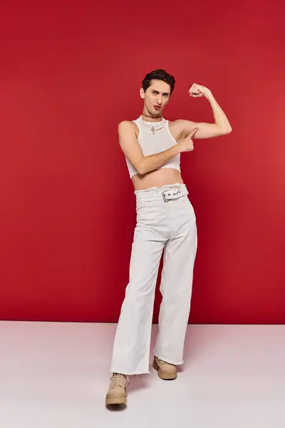 stock image appealing young lgbtq person in casual attire with accessories playing muscles and looking at camera