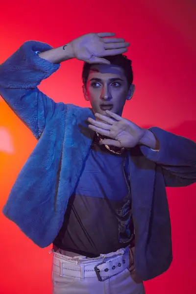 stock image attractive modish androgynous man in purple faux fur posing on vibrant backdrop and looking away