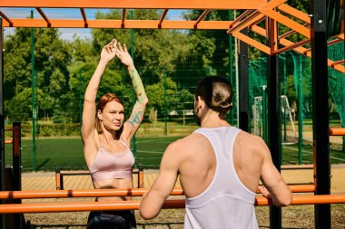 Spor kıyafetleri giymiş kararlı bir erkek ve kadın, hareketli bir park ortamında egzersiz yaparken sınırlarını zorluyorlar..