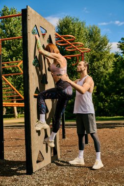 A determined woman, in sportswear, climbing an outdoor rock wall with personal trainer, showing motivation and teamwork. clipart