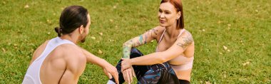 Spor giyimli bir erkek ve kadın çimlerin üzerinde birlikte oturuyorlar, spor yolculuklarında birlikteler. Kararlılık ve motivasyon yayarlar..
