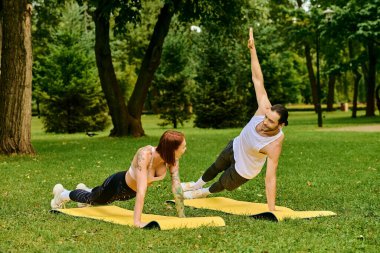 Spor kıyafetleriyle yoga yapan bir erkek ve kadın huzur parkında poz veriyorlar..