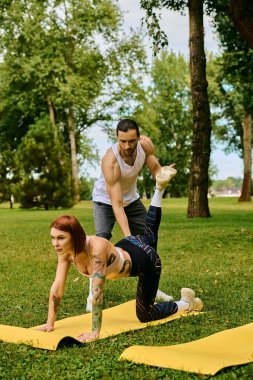 Spor giyimli bir kadın parkta özel antrenörle yoga yapıyor. Kararlılık ve motivasyon gösteriyor..